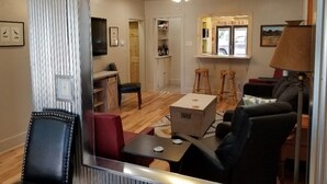Un salon doté d’un plancher en bois, d’un ventilateur de plafond, d’une télévision et d’un coin bar avec des tabourets.