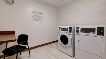 A guest laundry area with two washing machines, a chair, and a clock on the wall.