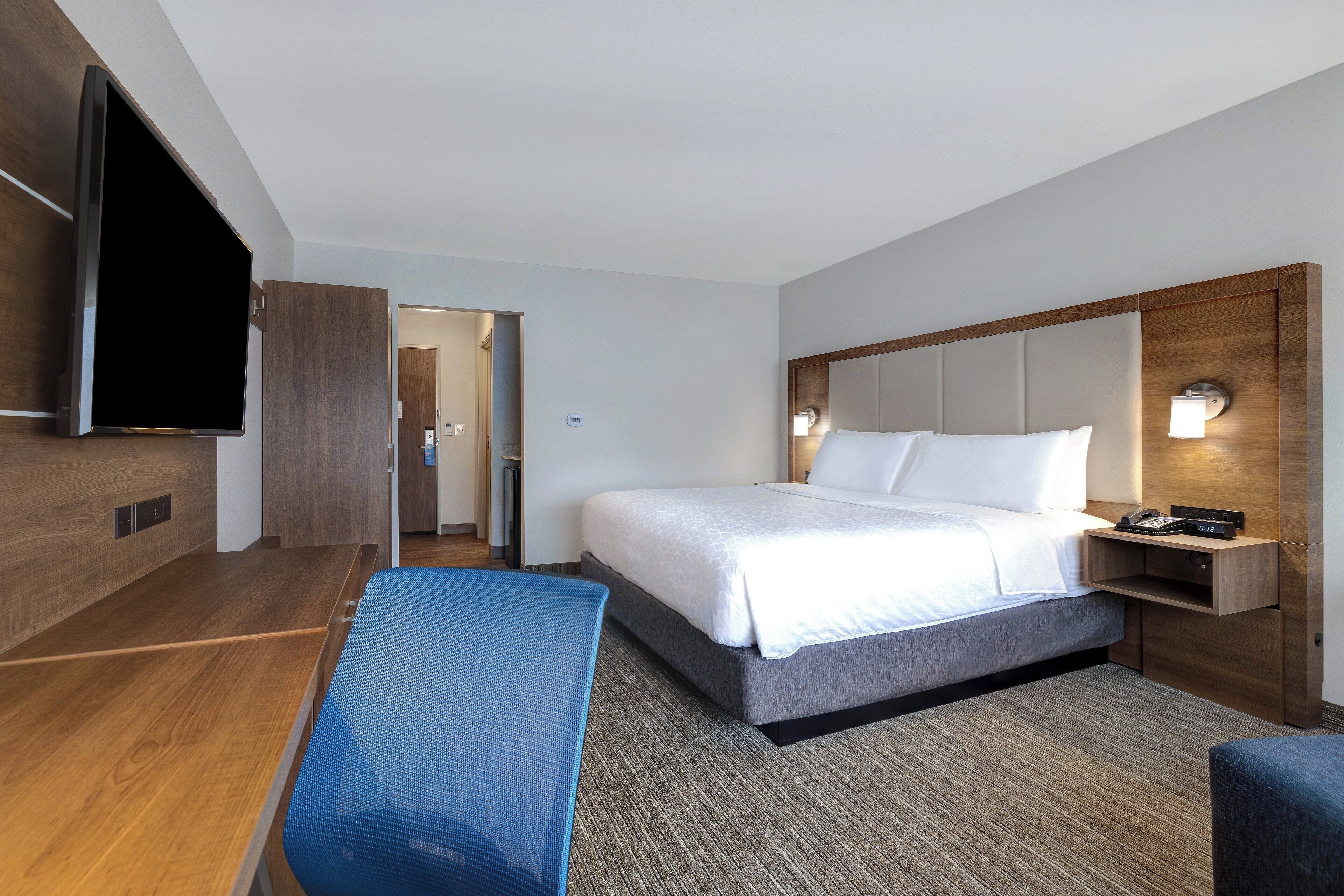 A modern hotel room with a large bed, a flat-screen TV mounted on the wall, and a desk with a chair.