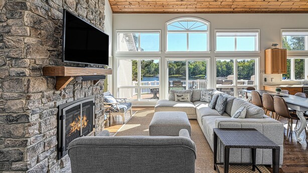 A spacious living room with a stone fireplace, large windows, and a view of a lake. - Resort-like LAKEFRONT 5br/4ba home & boathouse in quiet cove. Fun 4 all ages! (Bumpass)