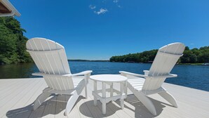 A deck with two Adirondack chairs and a small table, overlooking a body of water. - Resort-like LAKEFRONT 5br/4ba home & boathouse in quiet cove. Fun 4 all ages! (Bumpass)