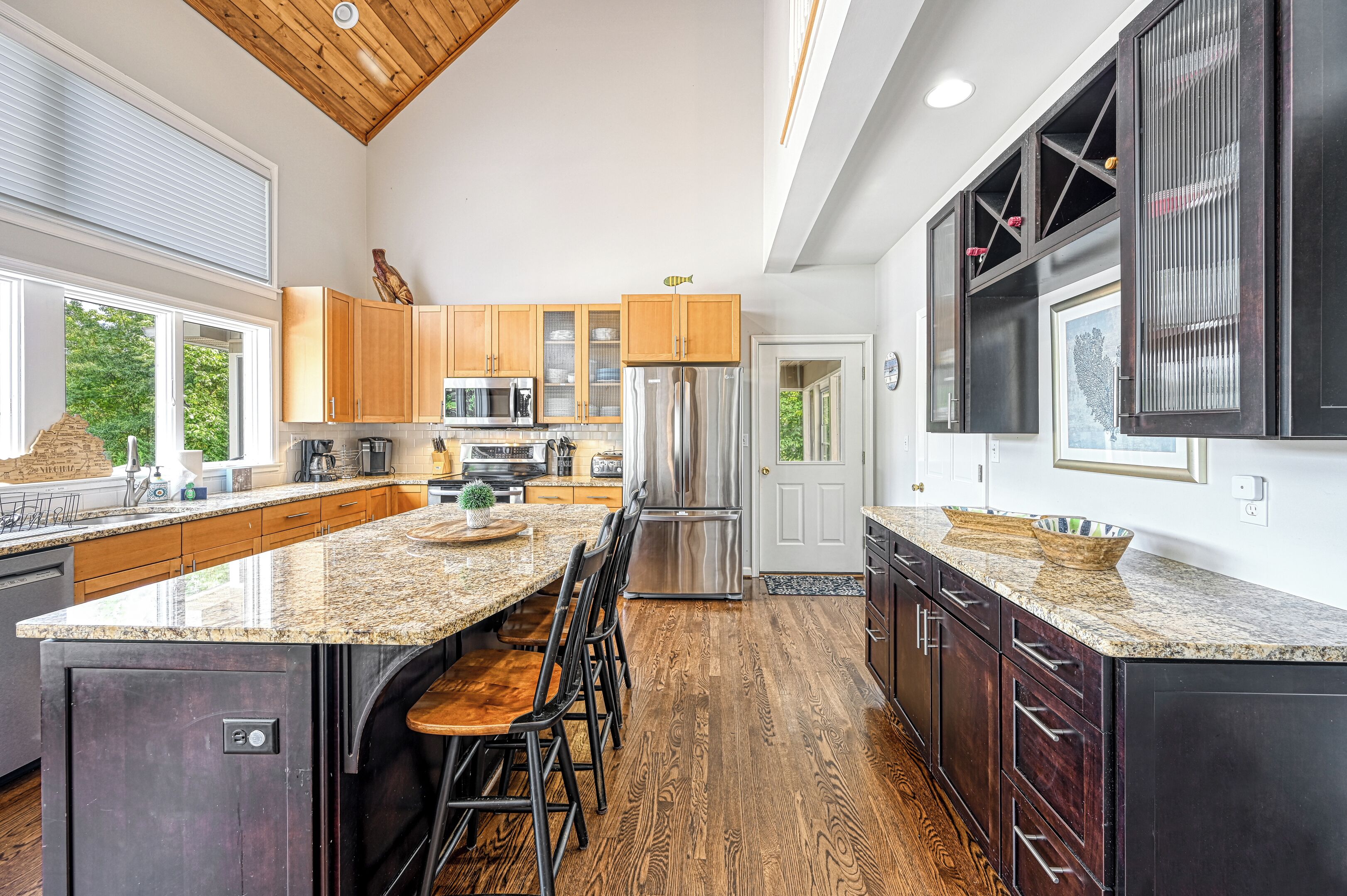 A spacious kitchen with a large island, wooden cabinets, stainless steel appliances, and a view of the outdoors.