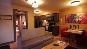 Un salon avec un canapé, une table à manger avec des chaises, un coin cuisine équipé d’un four à micro-ondes et un tableau accroché au mur.