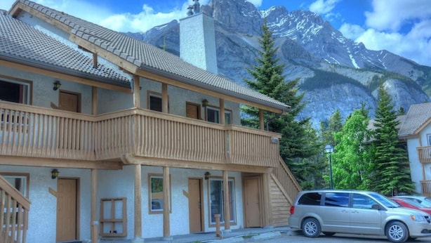 Un bâtiment à deux étages doté d’un balcon en bois, une voiture garée devant et une montagne en arrière-plan.