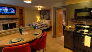 Une pièce confortable comprenant un lit, une table à manger avec des chaises, un téléviseur fixé au mur, une cheminée et un coin cuisine équipé d’une cuisinière et d’un four à micro-ondes.