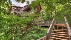Eine Holzhütte mit Balkon und Treppe, umgeben von üppigem Grün.