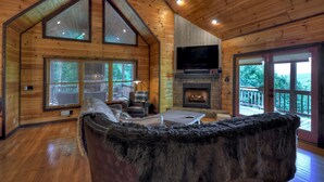 Ein gemütliches Blockhäuschen-Interieur mit Holzwänden, einem Kamin, einem Fernseher und einem großen, flauschigen Teppich.