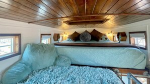 Un dormitorio con techo de madera, cama con ropa de cama estampada y una alfombra azul mullida.