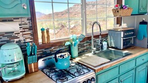 Una cocina con estufa a gas, cafetera y ventana con vistas a un paisaje desértico.