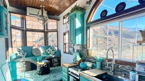 Una cocina con gabinetes color turquesa, una estufa y un lavabo. Se ve un ventanal con vistas a un paisaje montañoso.