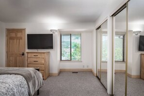 Quarto com cama, cômoda, televisão e guarda-roupa de portas deslizantes.