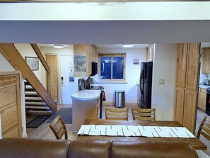 A dining area with a wooden table and chairs, a kitchen with wooden cabinets, and a staircase leading to another level.