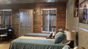 A room with a bed, a desk, and a chair. There are two doors and a window with blinds.