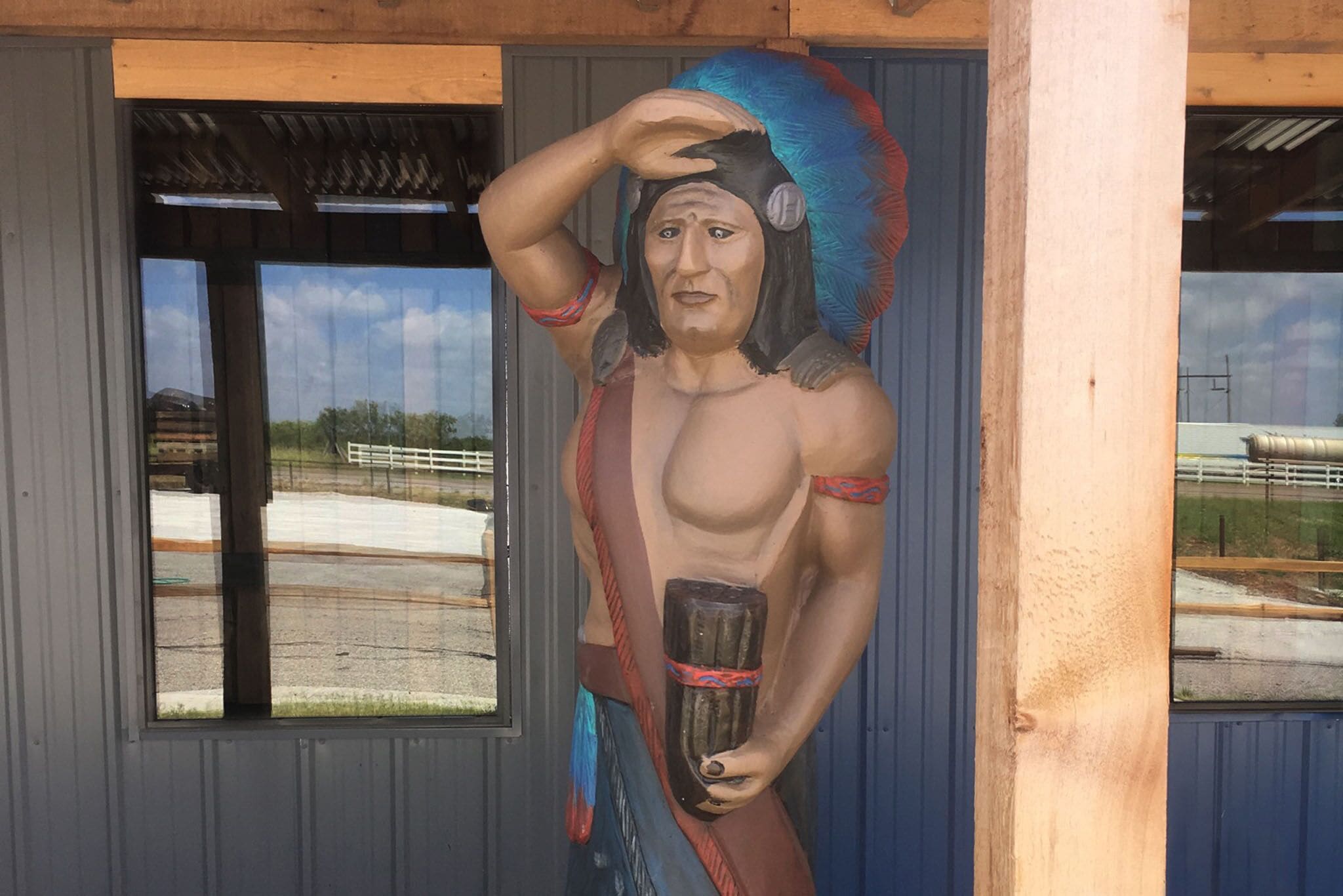 A mural of a Native American figure holding a pipe, set against a building facade with windows overlooking a road.