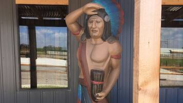 A mural of a Native American figure holding a pipe, set against a building facade with windows overlooking a road.