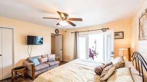 A bedroom with a bed, a ceiling fan, a TV, a sofa, and a sliding glass door leading to an outdoor area.