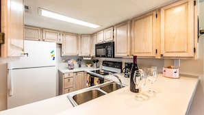 A modern kitchen with wooden cabinets, a white refrigerator, a black microwave, and a stainless steel sink.