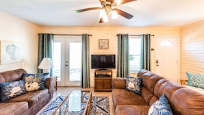 A living room with a ceiling fan, a flat-screen TV, two sofas, a coffee table, and a patterned rug.