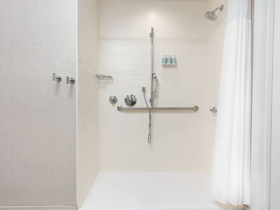 Un espace douche moderne doté d’une porte en verre, d’un pommeau de douche à main, d’un robinet mural et d’un porte-serviettes.