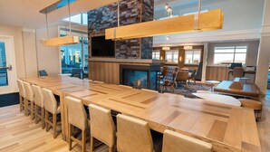 Un comedor amplio con una larga mesa de madera y sillas, una chimenea y una cocina moderna al fondo.