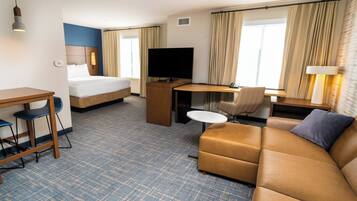 A hotel room with a bed, a desk with a television, a sofa, and a small table.