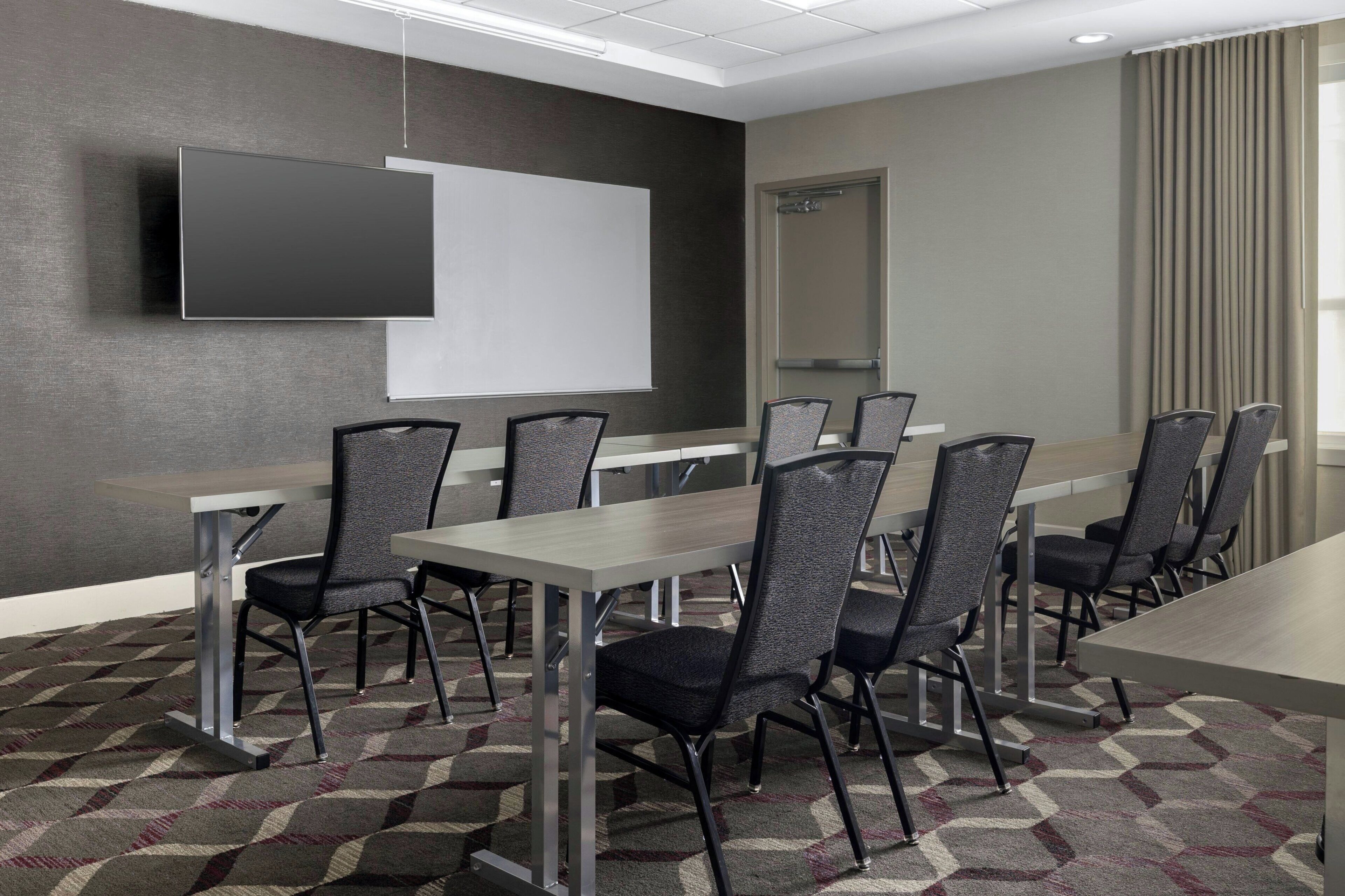 A conference room with a large table, six chairs, a whiteboard, and a flat-screen TV.