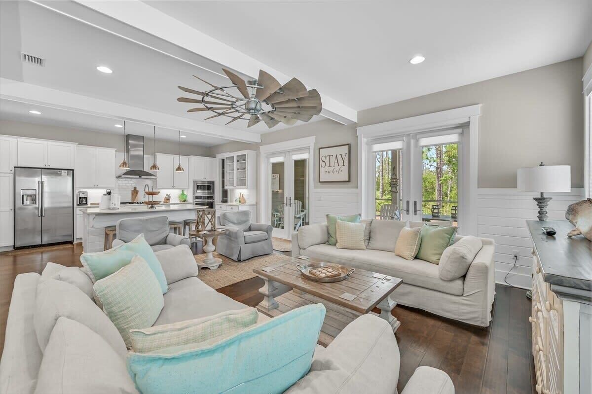 A spacious living area with a large ceiling fan, a kitchen with white cabinets, and a dining area with a table and chairs.