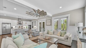 A spacious living area with a large ceiling fan, a kitchen with white cabinets, and a dining area with a table and chairs. - Golf Cart! Walk to the Pool & Beach! 3 Kings! 8 Bikes! Tons of Fun! Stay Awhile at NatureWalk on 30A (Santa Rosa Beach)