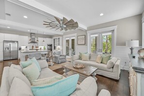 A spacious living area with a large ceiling fan, a kitchen with white cabinets, and a dining area with a table and chairs. - Golf Cart! Walk to the Pool & Beach! 3 Kings! 8 Bikes! Tons of Fun! Stay Awhile at NatureWalk on 30A (Santa Rosa Beach)