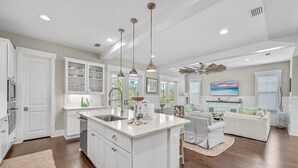 A spacious kitchen with white cabinetry, a central island, pendant lighting, and a view to a living area with a sofa and a painting. - Golf Cart! Walk to the Pool & Beach! 3 Kings! 8 Bikes! Tons of Fun! Stay Awhile at NatureWalk on 30A (Santa Rosa Beach)