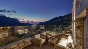Een balkon met rieten meubilair en een glazen hekwerk met uitzicht op een bergachtig landschap.