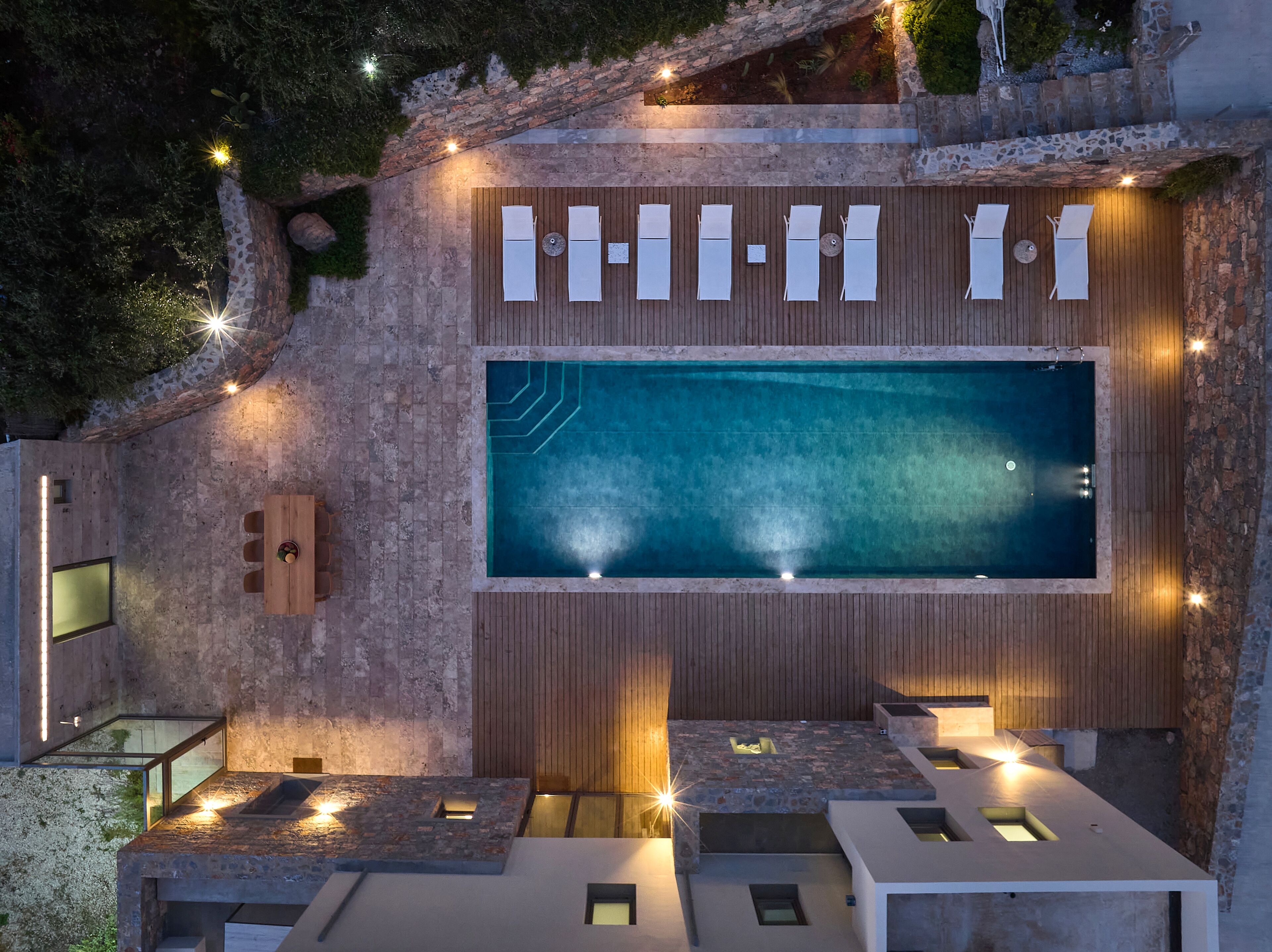 A rooftop pool area with a wooden deck, seating, and a large pool.
