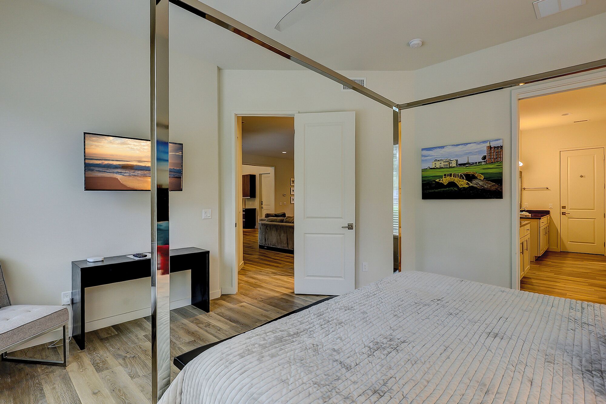A modern hotel room with a large bed, a desk with a computer, a flat-screen TV, and artwork on the walls.