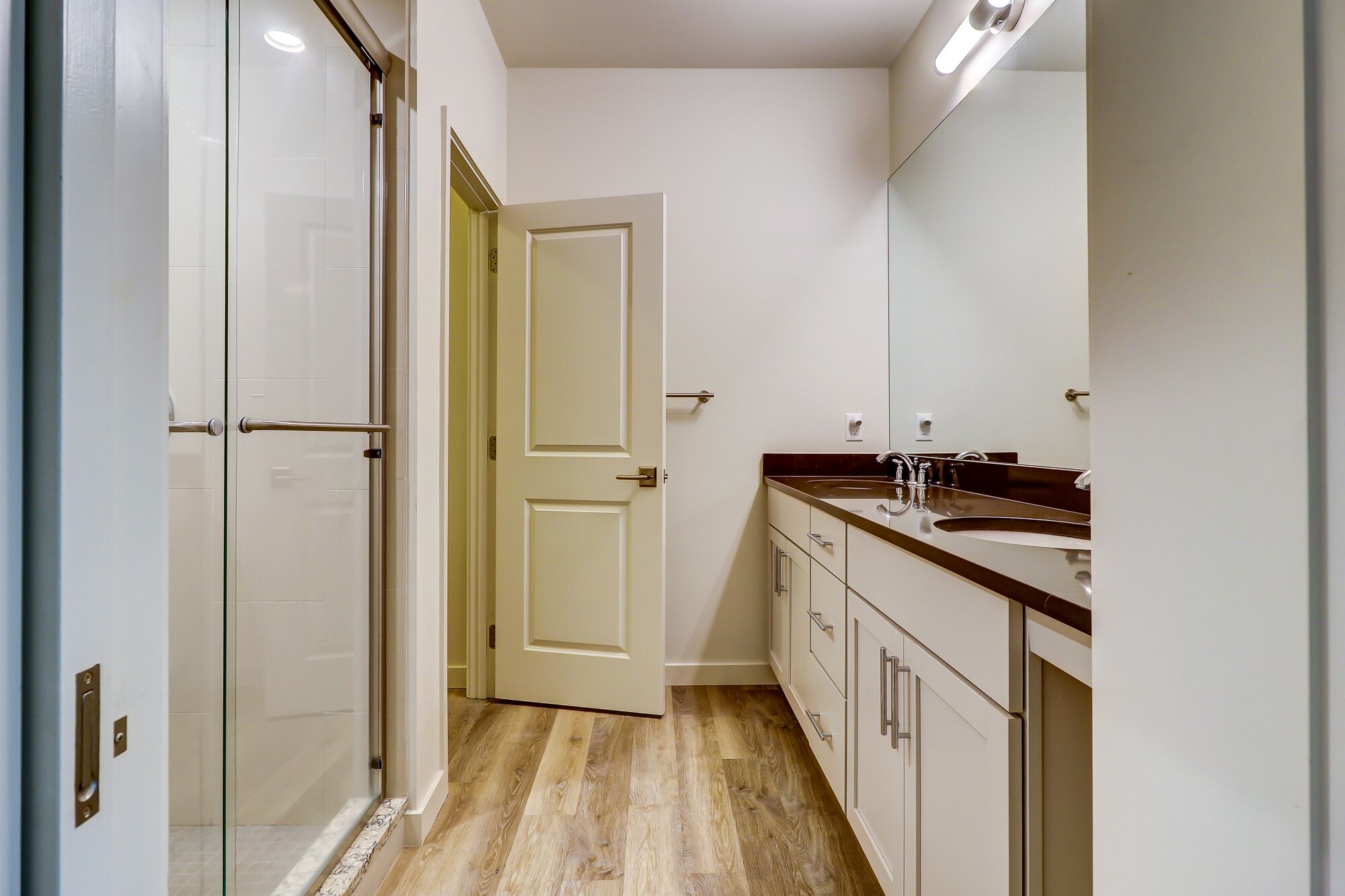 Un baño moderno con cabina de ducha de vidrio, puerta doble, lavabo con espejo y suelo de madera.