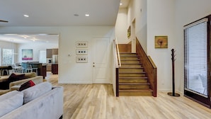Ein geräumiger Wohnbereich mit einer Holztreppe, einer Küche im Hintergrund und einem Essbereich mit modernen Möbeln.