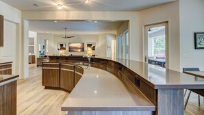 A modern kitchen with a curved island, wooden cabinets, and a large window providing natural light.