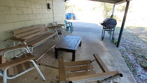 Un espace extérieur abrité, doté d’un sol en béton, de bancs en bois, d’une table et d’un barbecue.