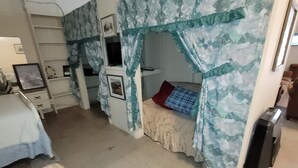 Une chambre avec un lit superposé, un bureau et une chaise. On y trouve un lit recouvert d’une couverture colorée et un tapis à motifs.
