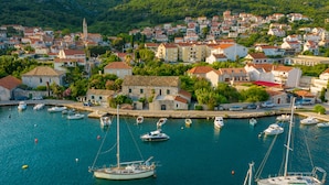 Un pueblo costero con un puerto deportivo lleno de barcos, rodeado de edificios residenciales y una imponente torre de iglesia.