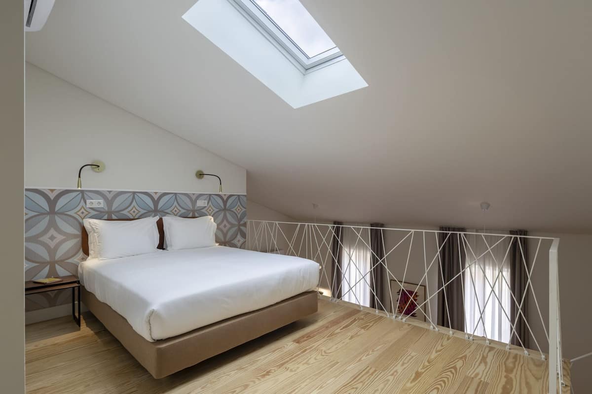 A bedroom with a skylight, a bed, a nightstand, and a patterned wall.