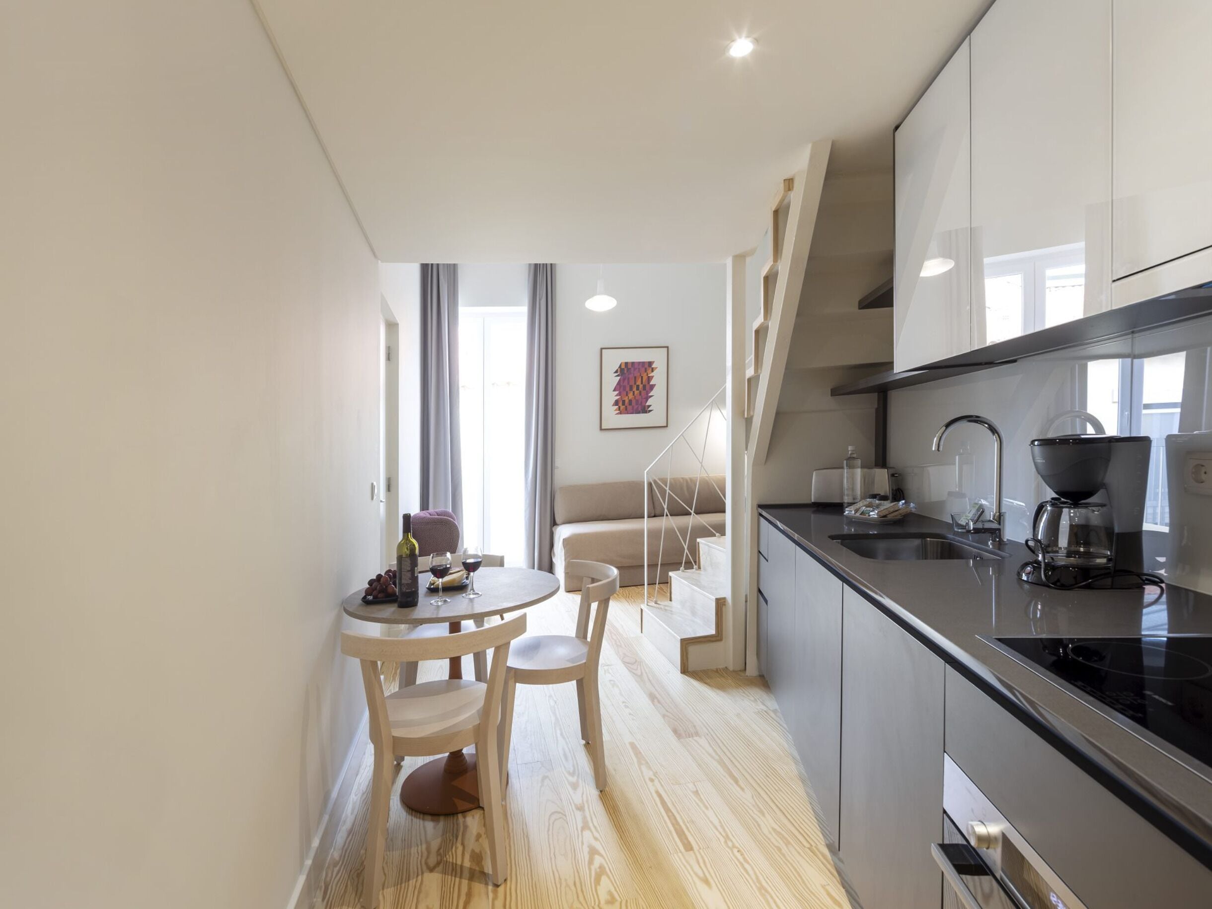 A modern kitchen with a dining area, wooden flooring, and a staircase leading to an upper level.