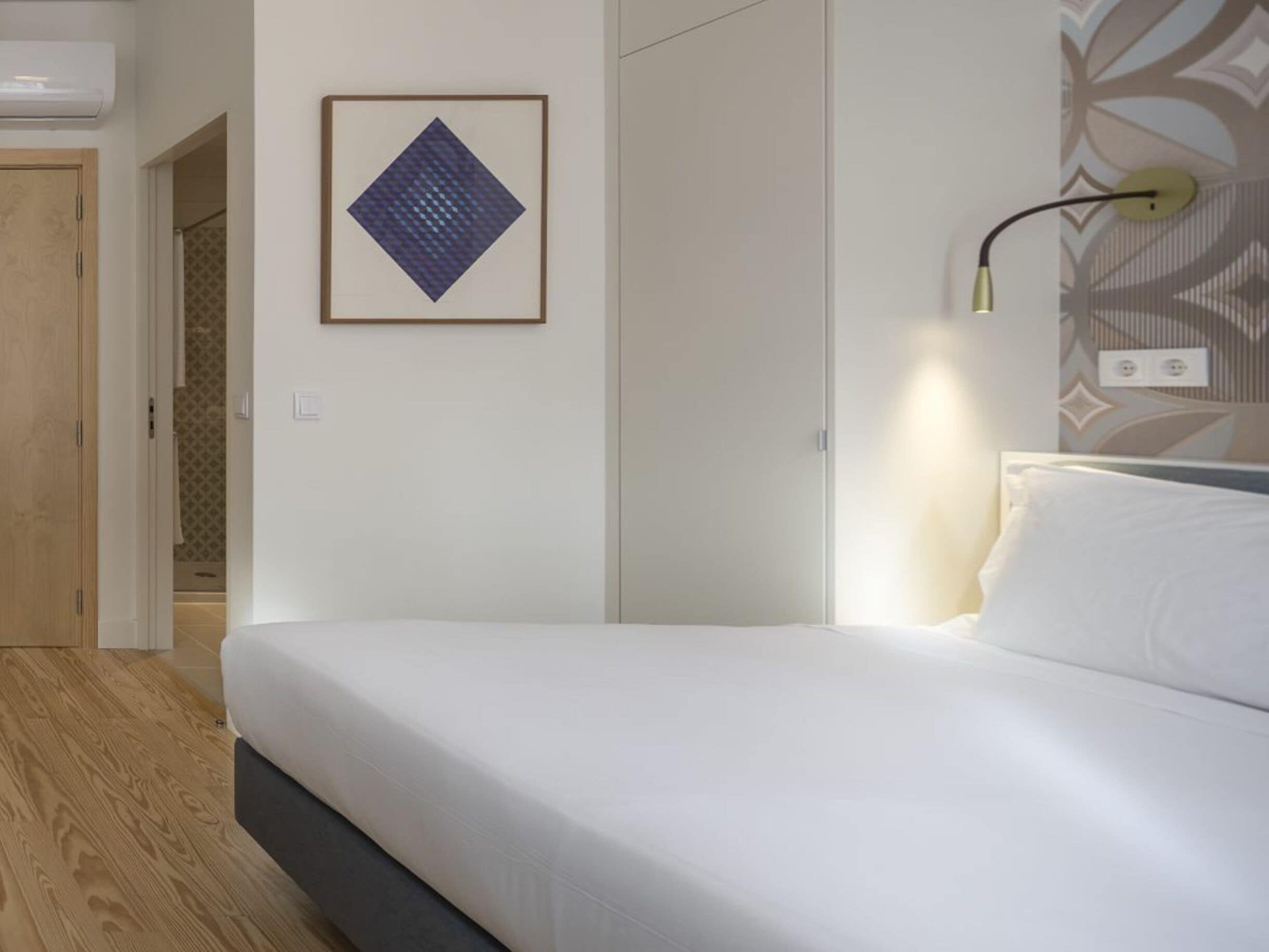 Une chambre à coucher comprenant un lit, une lampe fixée au mur, un tableau encadré et une armoire.