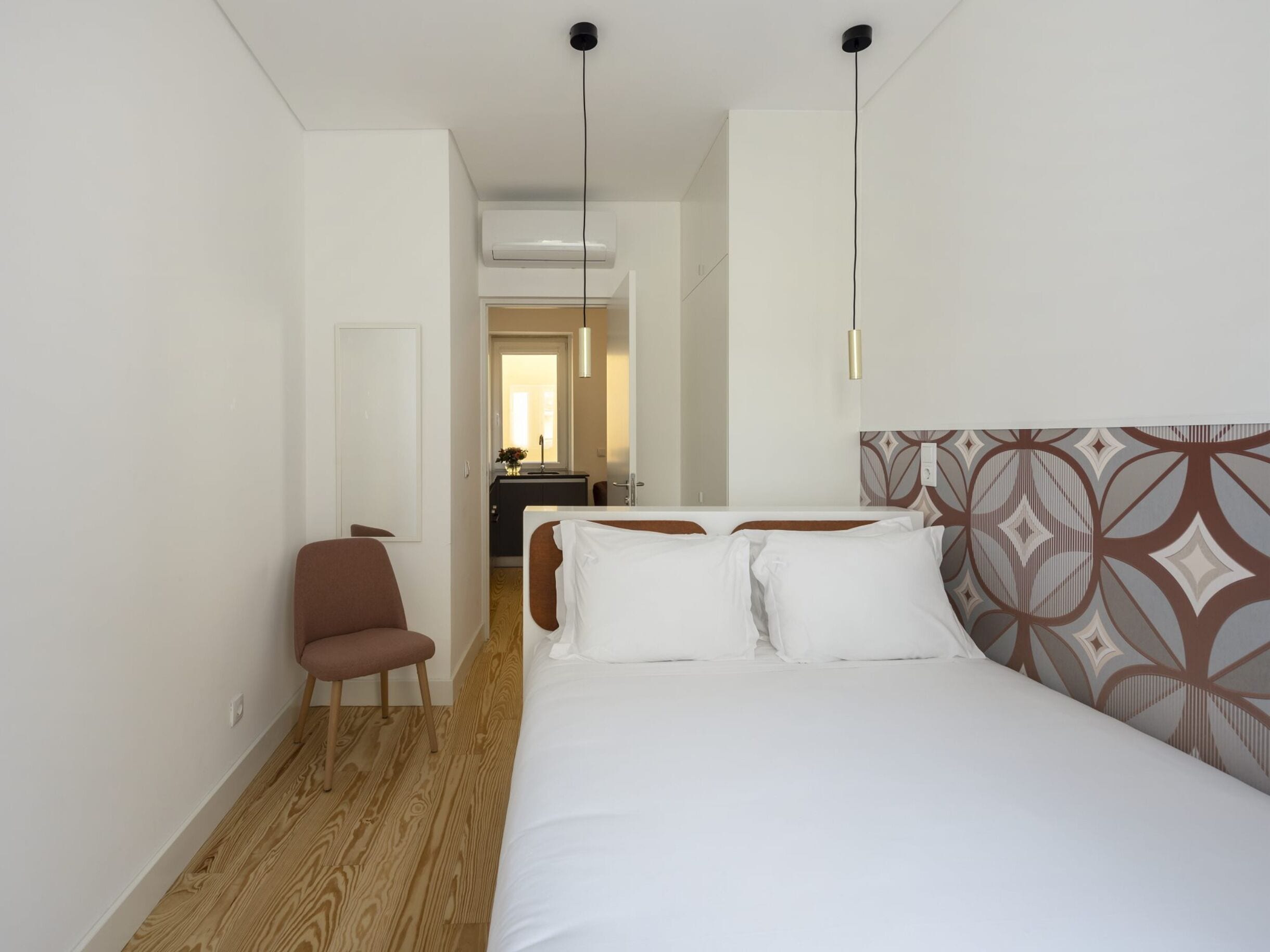Una habitación de hotel con cama, una silla, un escritorio y un equipo de aire acondicionado.