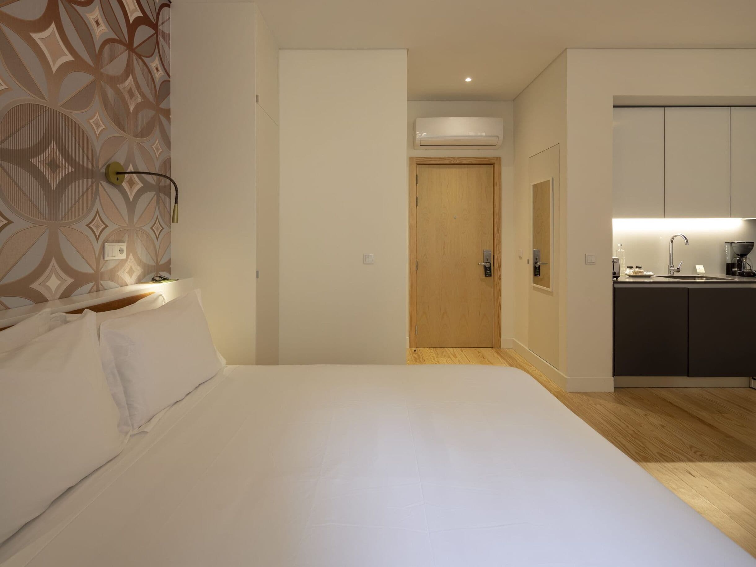 Ein Hotelzimmer mit Bett, Holztür, Küchenzeile und Wand mit Muster.
