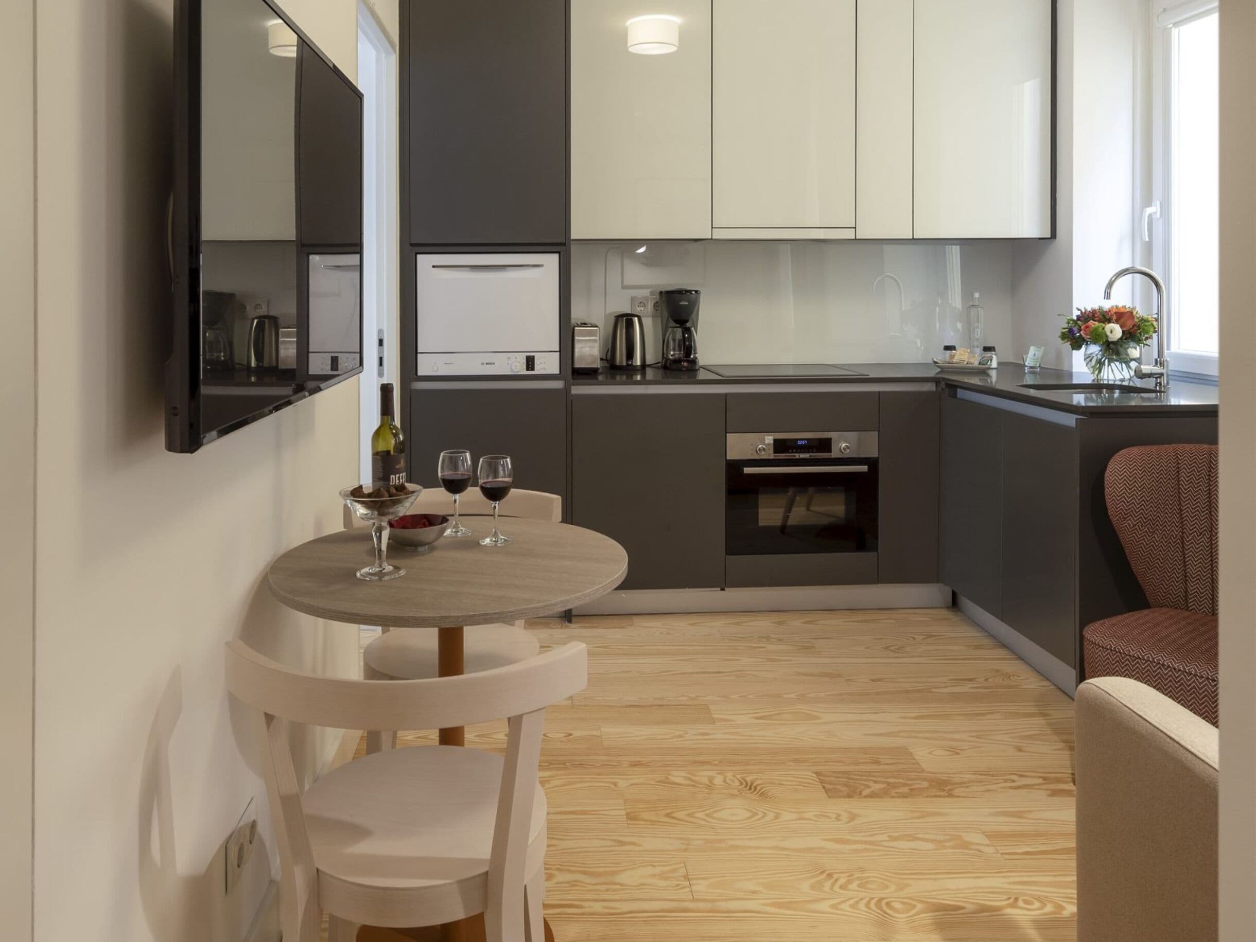 Uma cozinha moderna com área de refeições, incluindo uma mesa com cadeiras, uma cafeteira e uma taça de vinho.