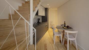 A modern kitchen with wooden flooring, a dining area with white chairs, and a staircase with wooden steps.