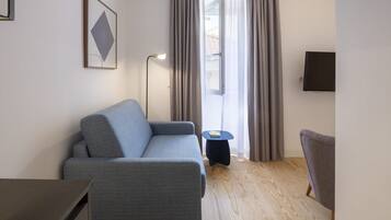Una sala de estar moderna con un sofá gris, una mesita auxiliar, una silla, una lámpara de pie y un televisor montado en la pared.