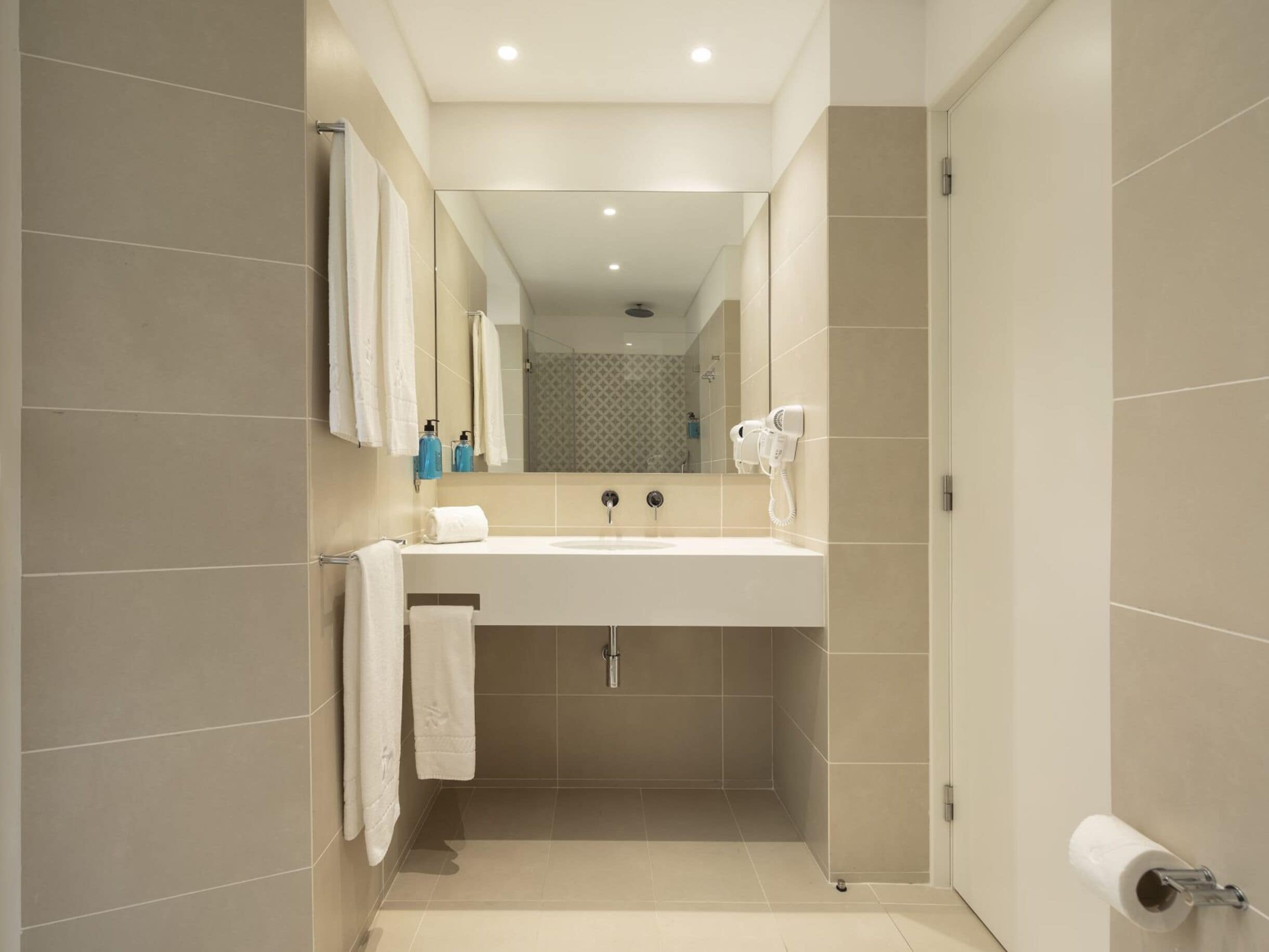 Un baño moderno con un espejo grande, un lavabo, un perchero para toallas y un secador de pelo.