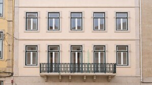 Een meerlaags gebouw met een balkon op de tweede verdieping, een gelijkvloerse ingang met een zwart luifel en een bord met een logo.