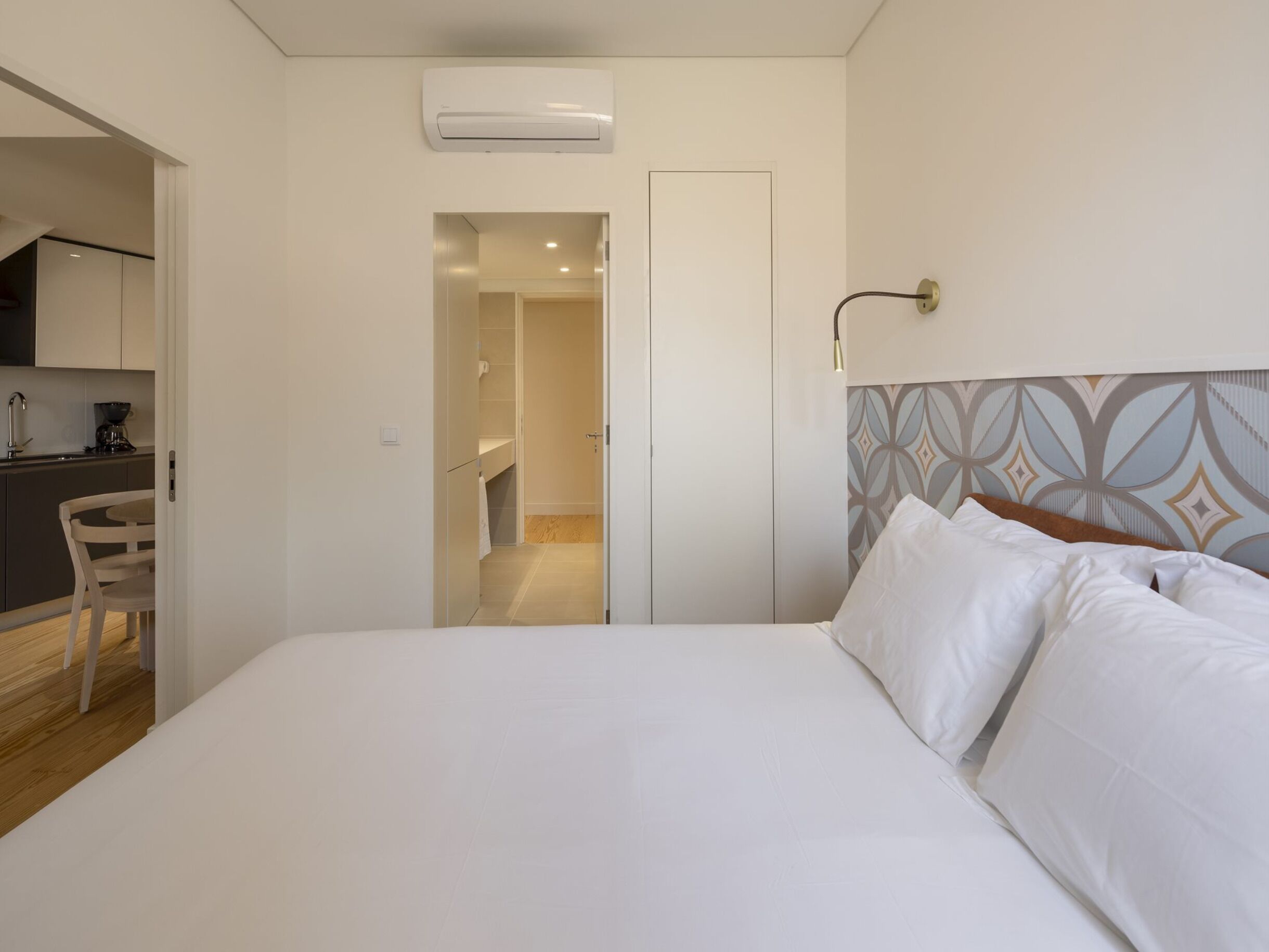Een hotelkamer met een bed, nachtkastje, stoel, kitchenette en badkamer.